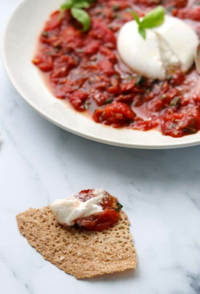 A plate of grilled tomatoes and burrata with a piece of crispbread