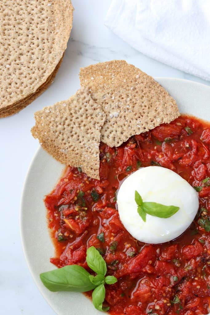 A plate with grilled tomatoes, basil, burrata and crispbread