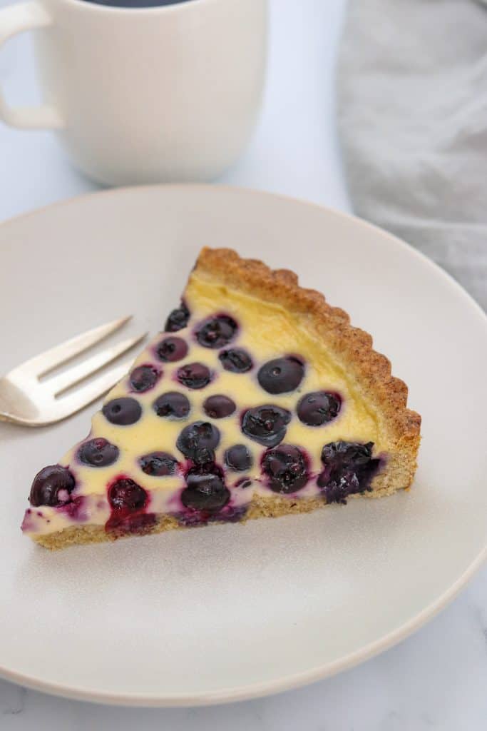 A close up of a slice of blueberry tart on a plate with a fork