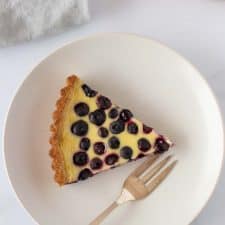 A slice of blueberry tart on a plate with a napkin and fork