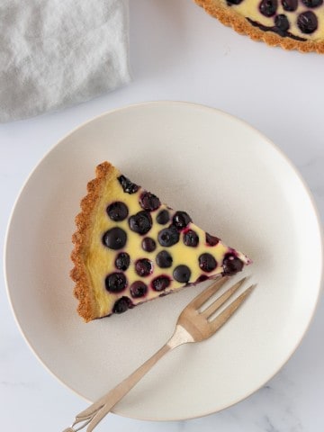 A slice of blueberry tart on a plate with a napkin and fork