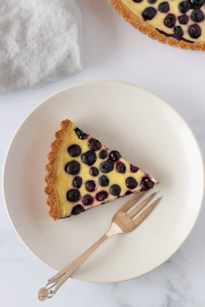 A slice of blueberry tart on a plate with a napkin and fork