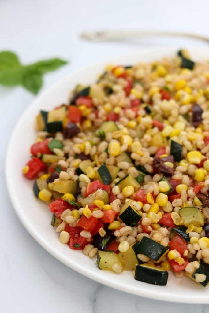 A plate of barley salad with corn, zucchini and tomatoes