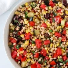 A bowl of barley salad with corn, zucchini and tomatoes