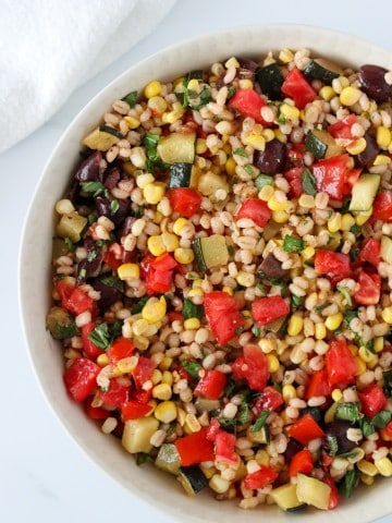 A bowl of barley salad with corn, zucchini and tomatoes