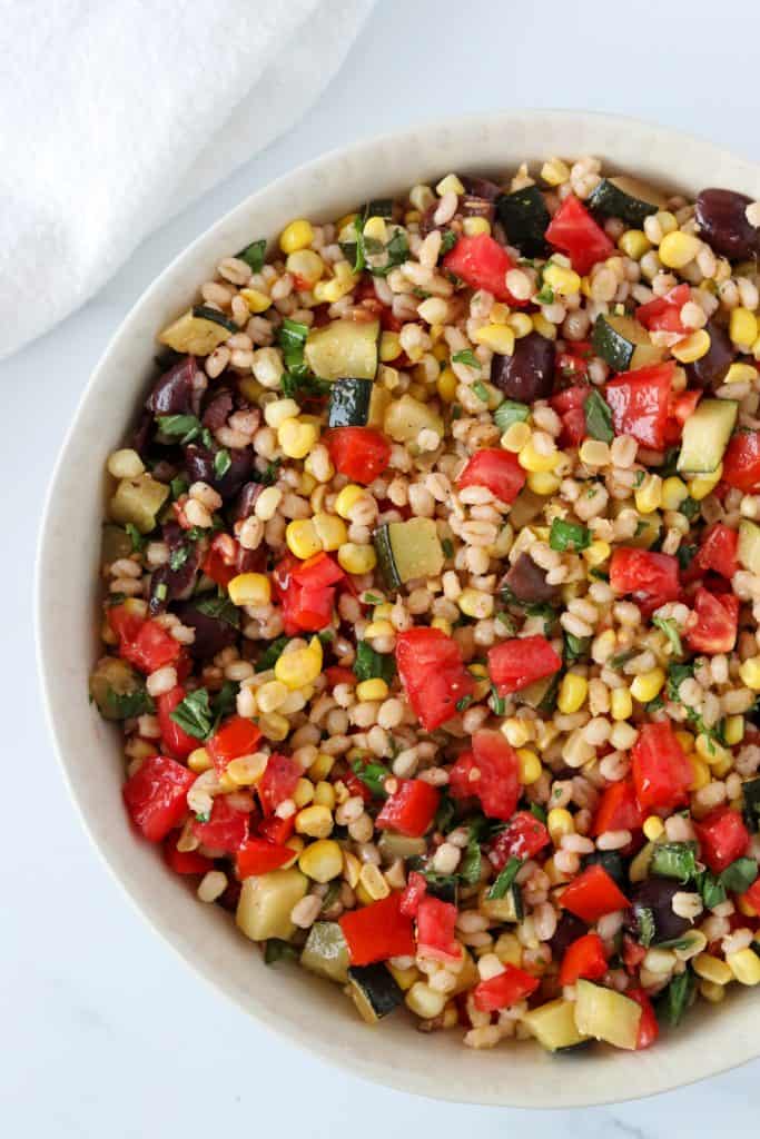 A bowl of barley salad with corn, zucchini and tomatoes