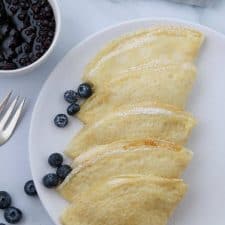 A plate of Swedish pancakes with blueberries and a fork
