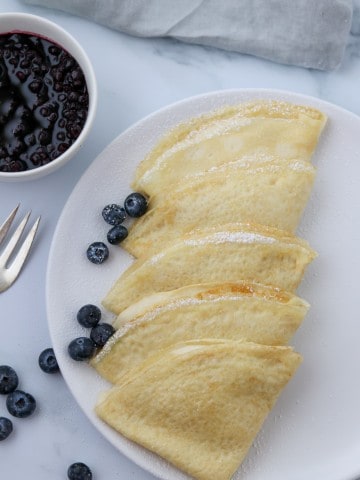 A plate of Swedish pancakes with blueberries and a fork