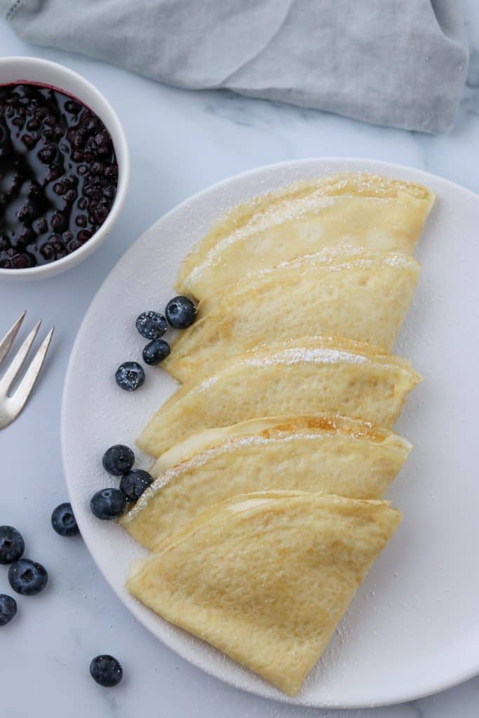 A plate of Swedish pancakes with blueberries and a fork