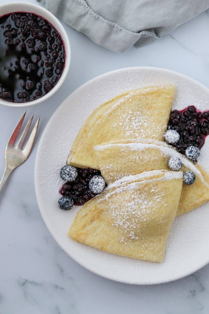 A plate of Swedish pancakes with blueberries and a fork