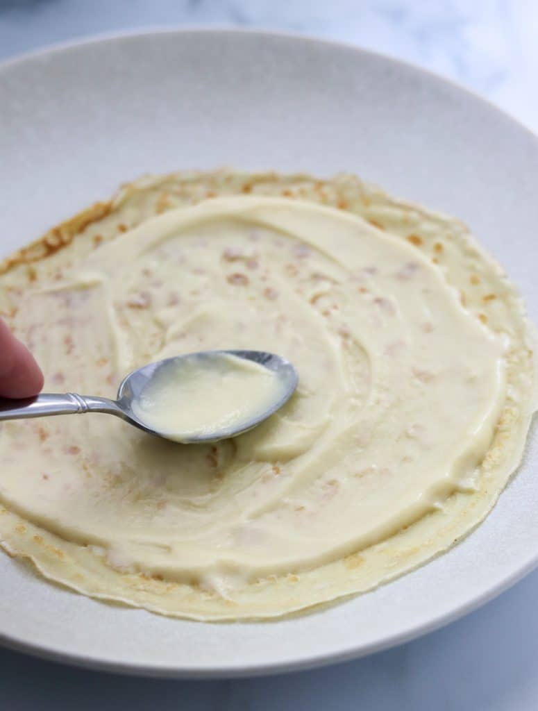 A Swedish pancake topped with vanilla pastry cream on a plate with a spoon 