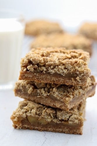 A close up of a stack of apple crumble bars with a glass of milk