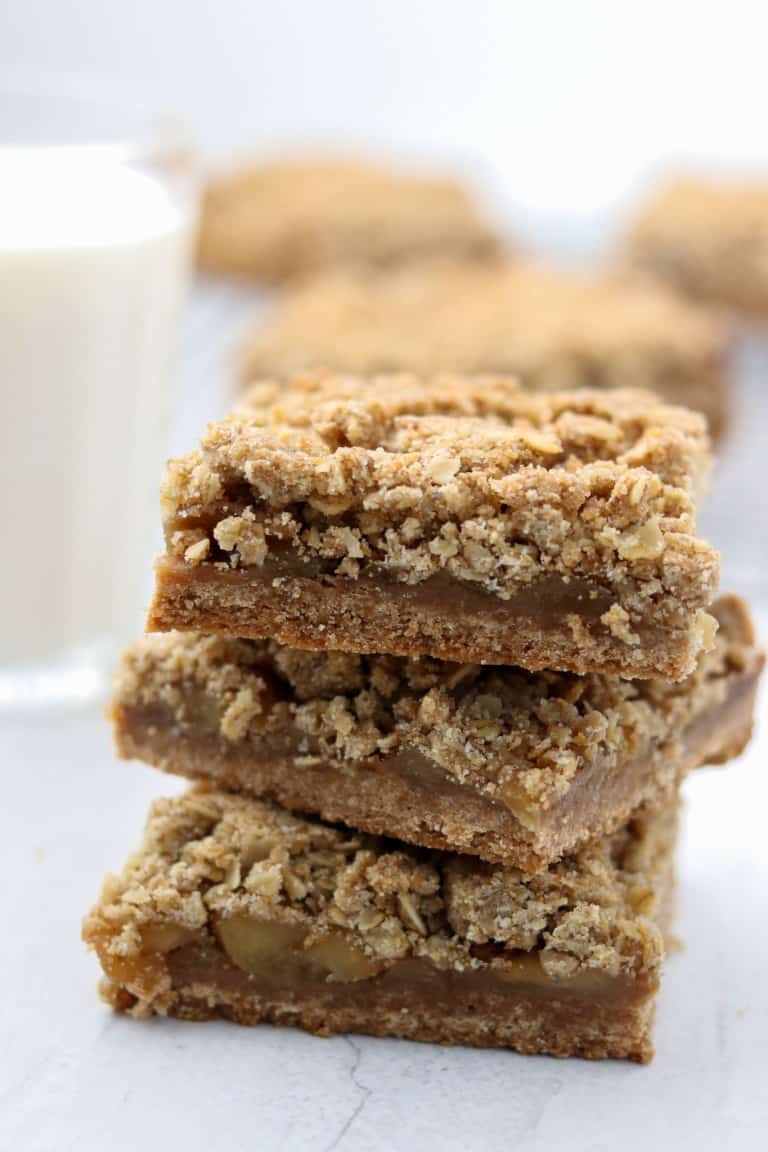 A close up of a stack of apple crumble bars with a glass of milk