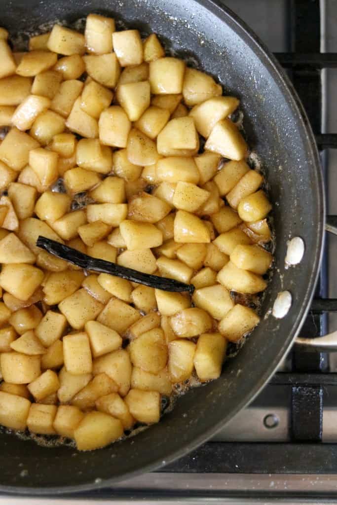 Cubes of apple and a vanilla bean cooking in a skillet