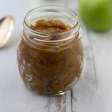 Caramelized apple compote in a jar next to a spoon and apples