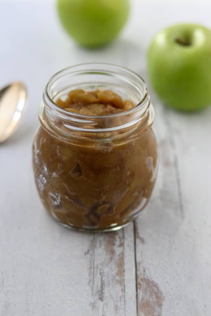 Caramelized apple compote in a jar next to a spoon and apples