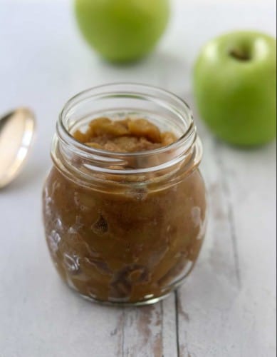Caramelized apple compote in a jar next to a spoon and apples