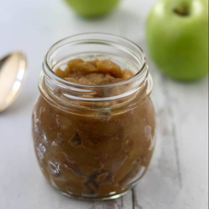 Caramelized apple compote in a jar next to a spoon and apples