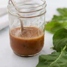 A close up of a jar of vinaigrette with a spoon