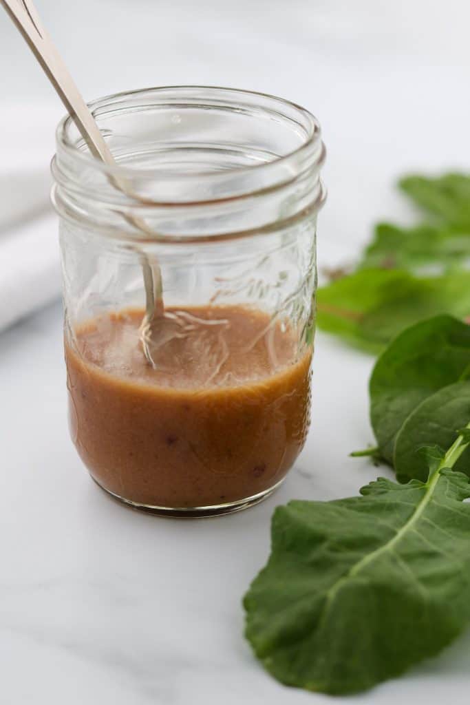 A close up of a jar of vinaigrette with a spoon