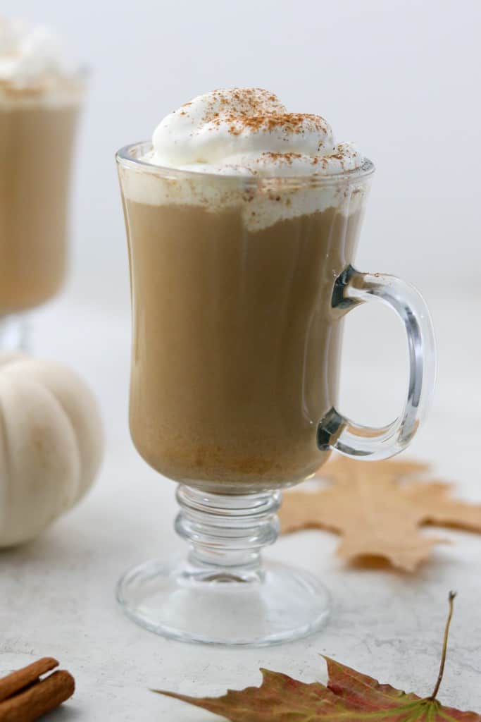 Pumpkin spice latte in a glass mug with fall leaves