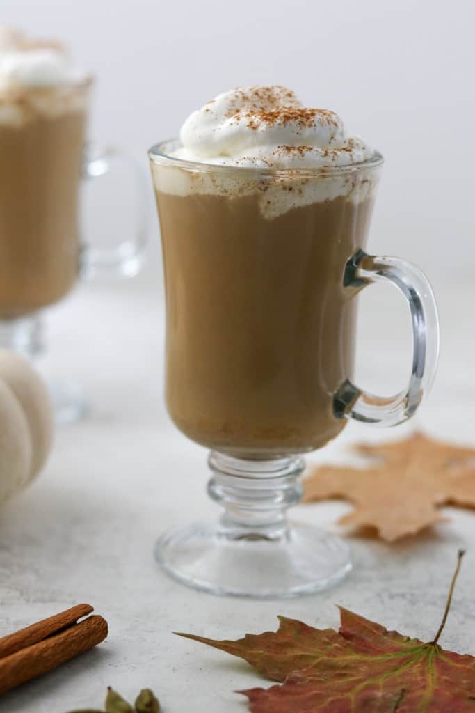 Pumpkin spice latte in a glass mug with fall leaves