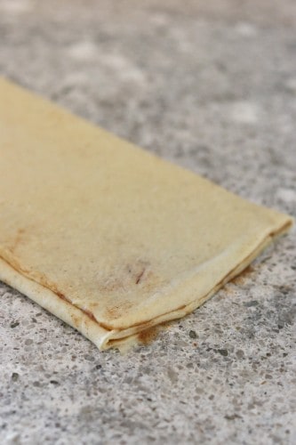 Folded cinnamon bun dough on a gray countertop