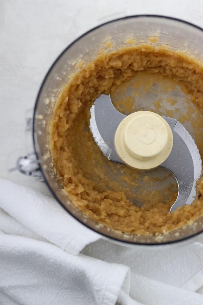 Applesauce in the work bowl of a food processor next to a white towel