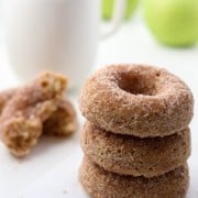 Close up of stack of three apple donuts next to a cup of coffee and apples