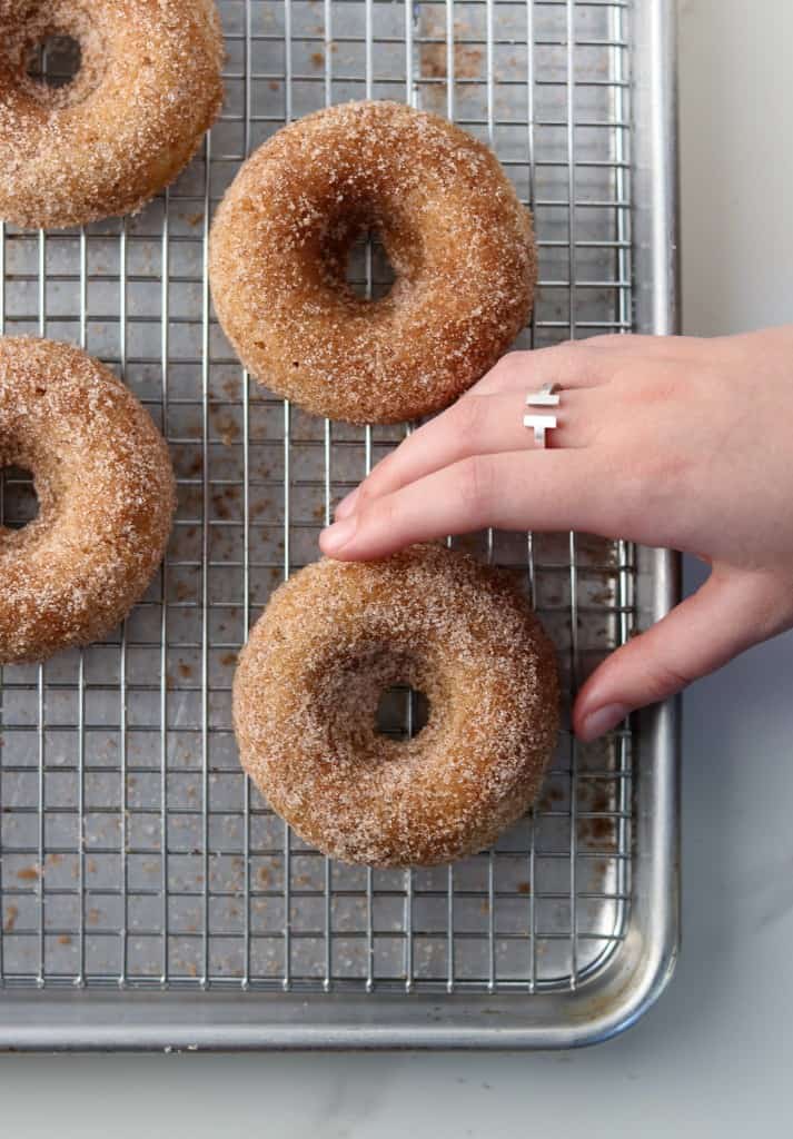 Hand reaching for baked apple donut on a cooling rack