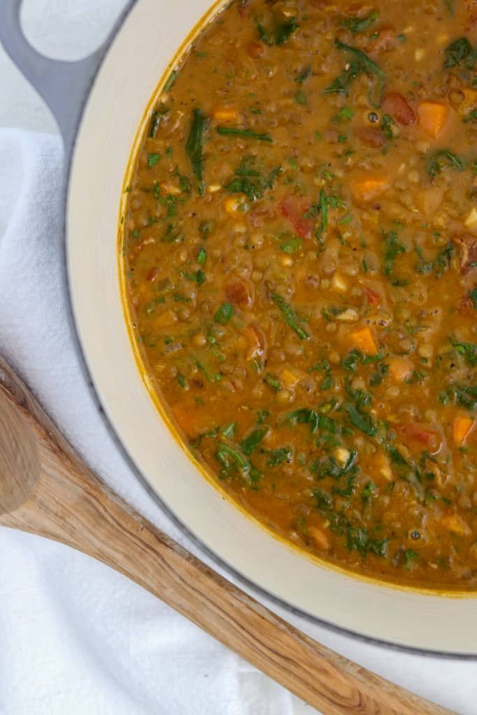 Hearty Lentil Soup with Roasted Butternut Squash, Kale and Bacon in a pot next to a wooden ladle