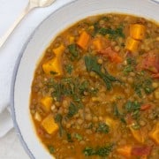 Close up of a bowl of Hearty Lentil Soup with Roasted Butternut Squash, Kale and Bacon next to a spoon and napkin