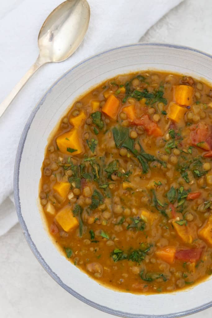 Close up of a bowl of Hearty Lentil Soup with Roasted Butternut Squash, Kale and Bacon next to a spoon and napkin