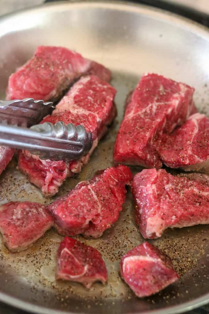 Beef cooking in a skillet with tongs