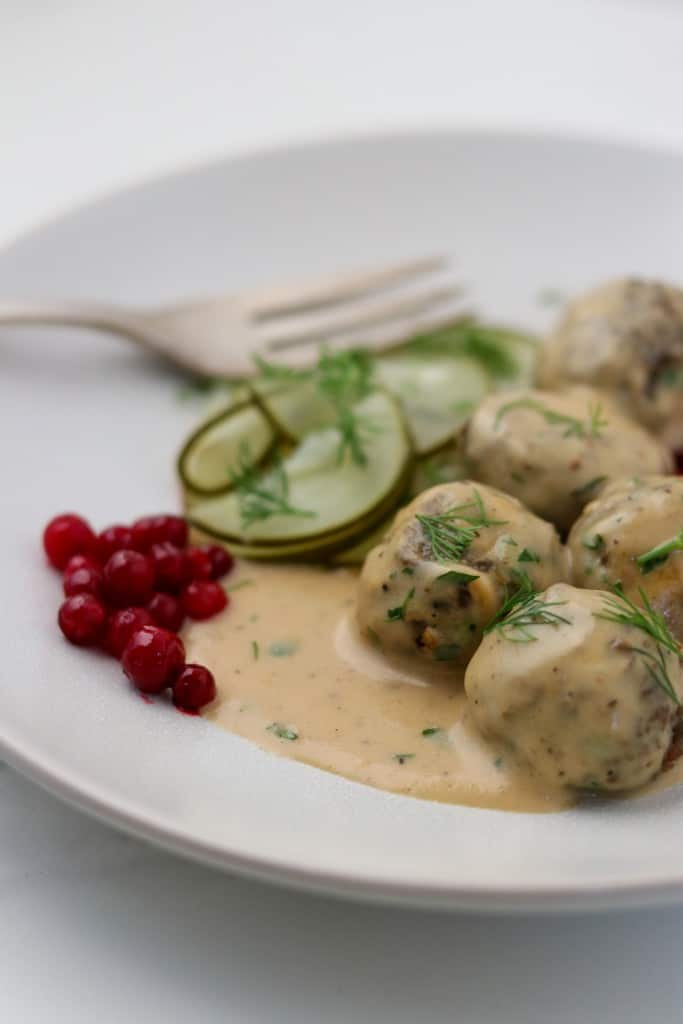 Close up of vegetarian meatballs in cream sauce with lingonberries and pickles
