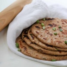 Flatbreads stacked on a towel next to a rolling pin