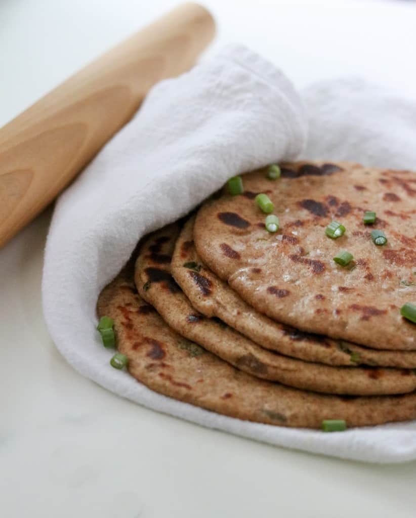 Flatbreads stacked on a towel next to a rolling pin