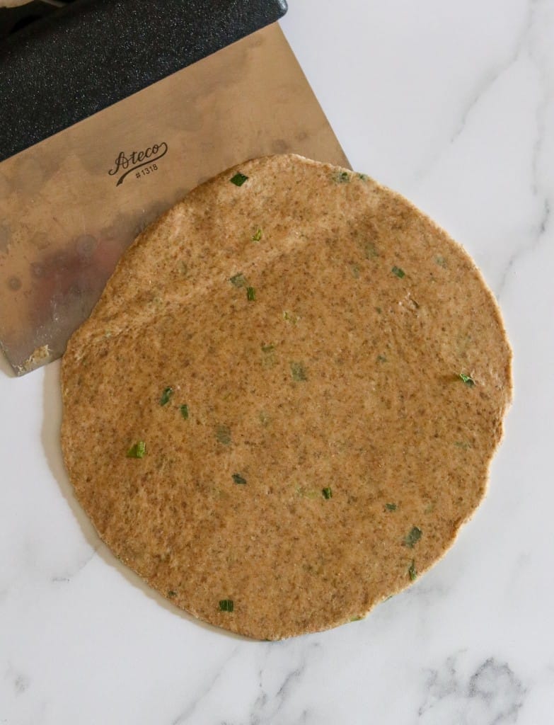 Flatbread dough rolled out on a counter with a dough scraper