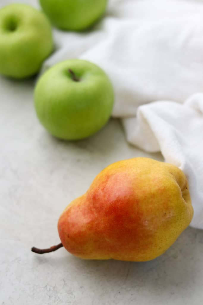 A pear and three apples next to a kitchen towel