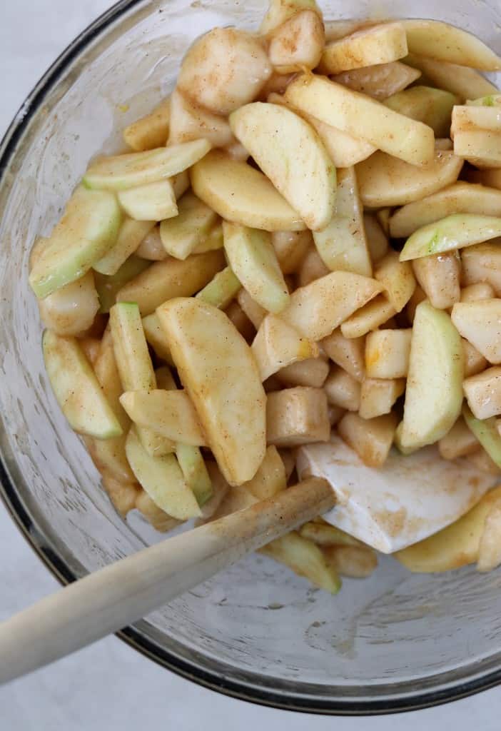 A bowl of sliced apples and pears tossed in spices with a rubber spatula