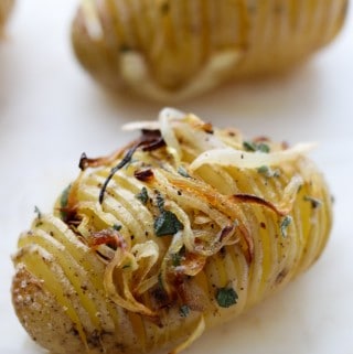 Close up of a hasselback potato topped with herbs and caramelized onions