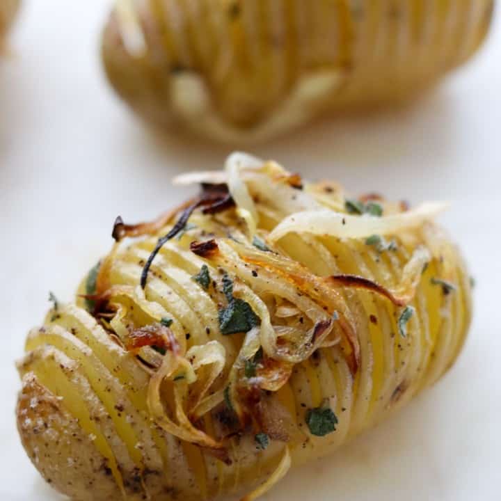 Close up of a hasselback potato topped with herbs and caramelized onions