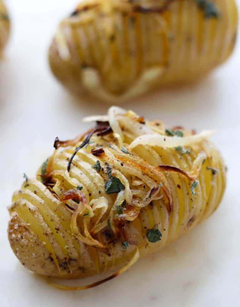 Close up of a hasselback potato topped with herbs and caramelized onions
