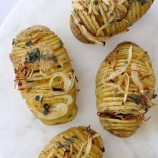 Hasselback potatoes topped with herbs and onions on a marble surface
