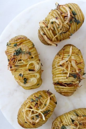 Hasselback potatoes topped with herbs and onions on a marble surface