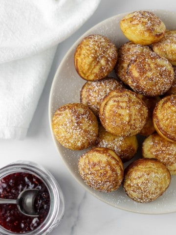 Æbleskivers on a plate next to jam and a napkin.