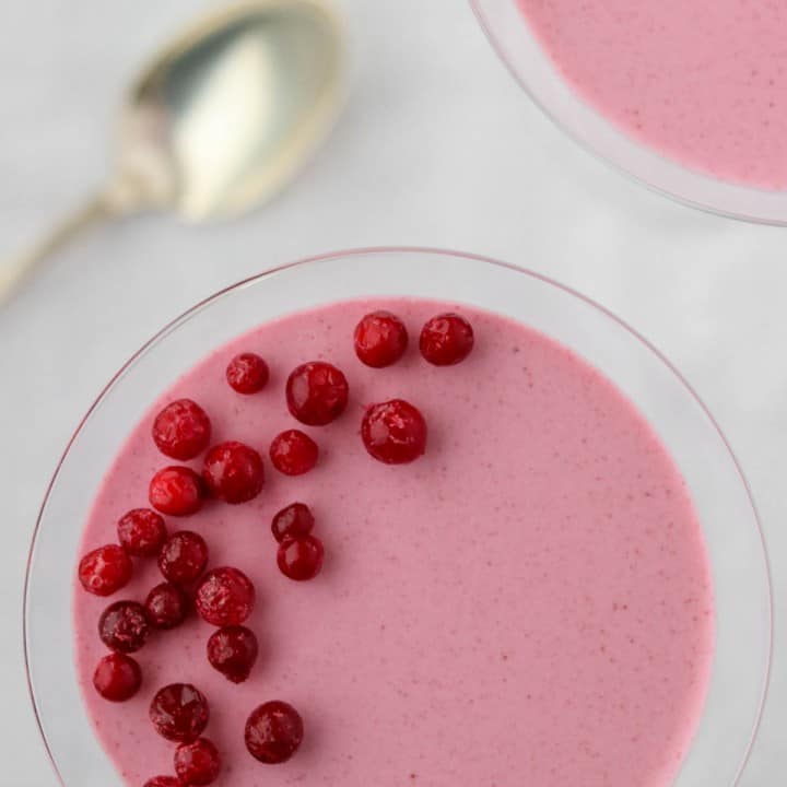 Lingonberry mousse in a glass next to a spoon.