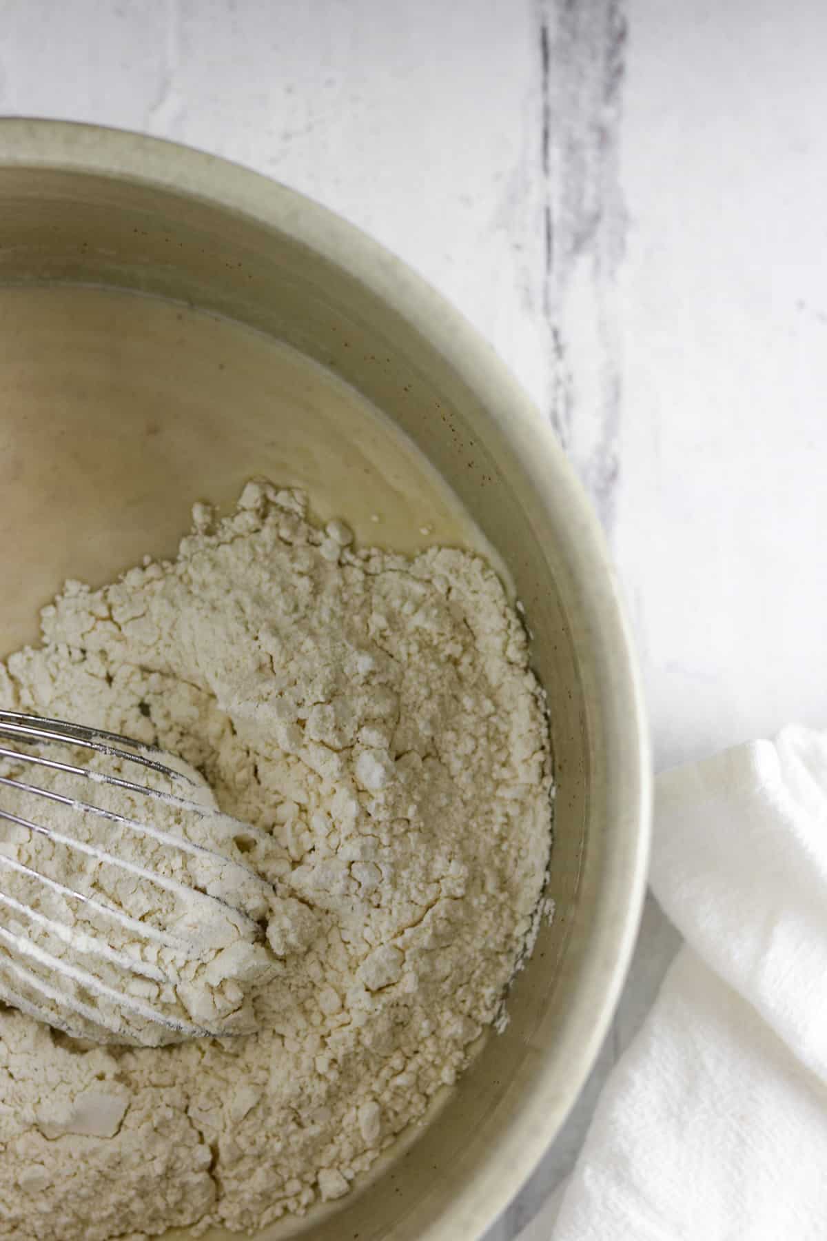 Flour in a bowl with a whisk on a wood background.