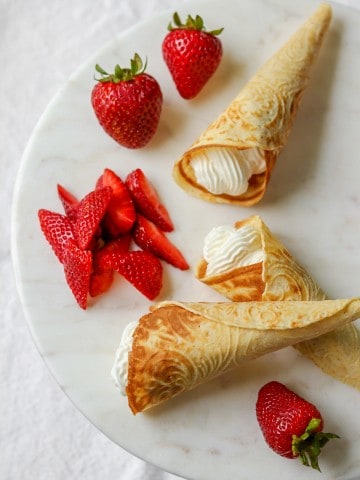 Krumkake filled with whipped cream and strawberries on a plate.