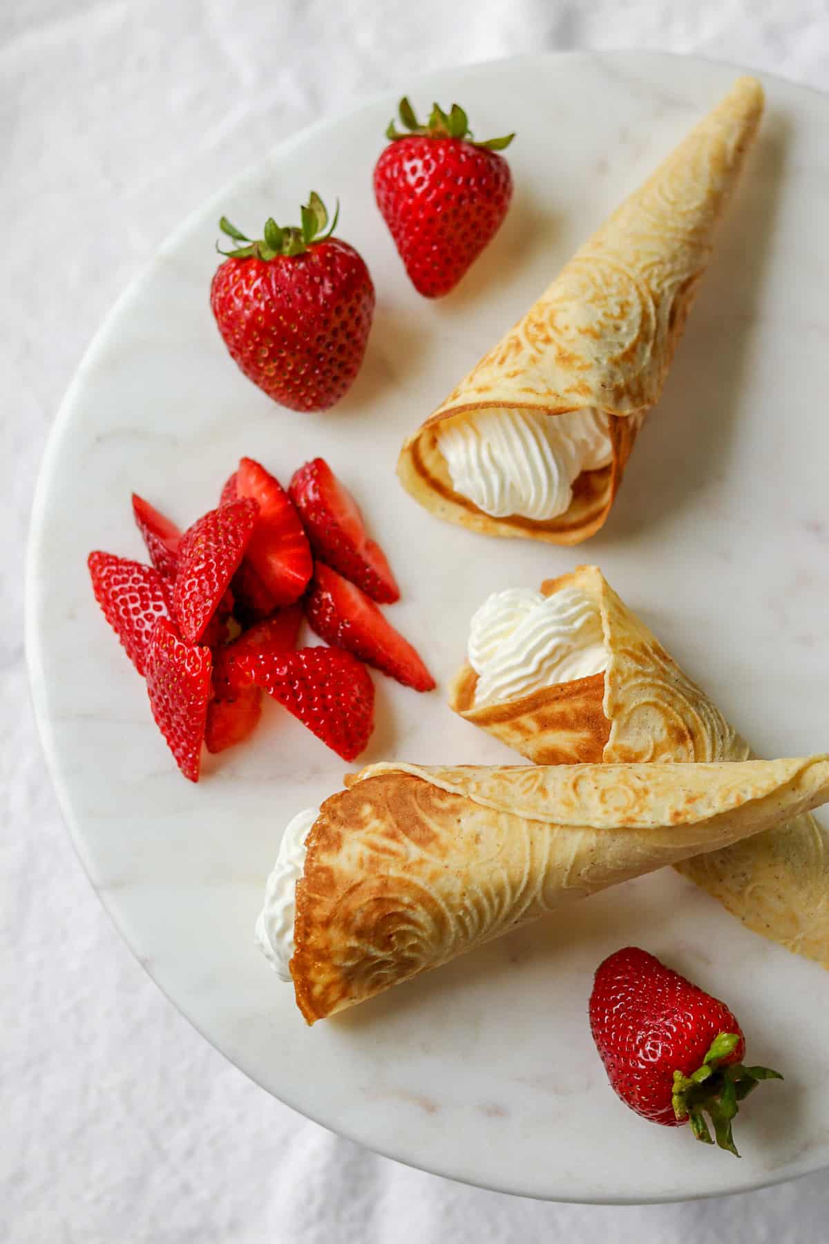 Krumkake filled with whipped cream and strawberries on a plate.